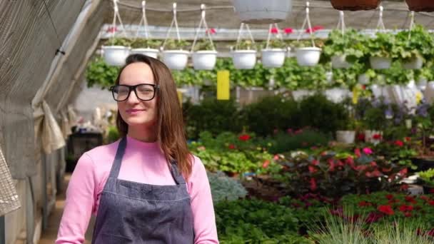 Porträt einer attraktiven lächelnden Gärtnerin in einem Gewächshaus mit Blumen. Gartenbau, Menschen und Konzept für den Blumenanbau. — Stockvideo