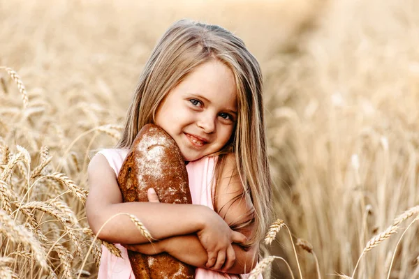 Gelukkige kleine meisje kind in tarwe graanveld in de zomer. Kinderen met brood. Klein meisje in het graanveld. Meisje op het veld van tarwe met brood — Stockfoto