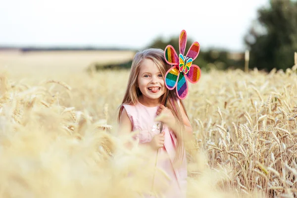 Menina feliz segurando brinquedo vento correndo no campo de trigo, alegrando a vida, felicidade — Fotografia de Stock