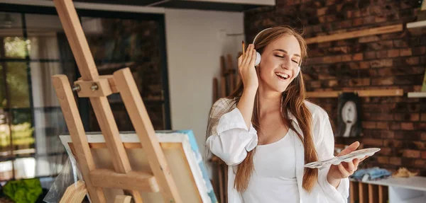 Sonriente señorita joven escuchando música y pintura, disfrutando de la terapia artística. —  Fotos de Stock