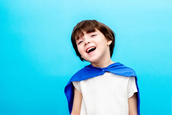Junge im Superhelden-Umhang lächelt vor Himmelshintergrund, glückliche Kindheit — Stockfoto