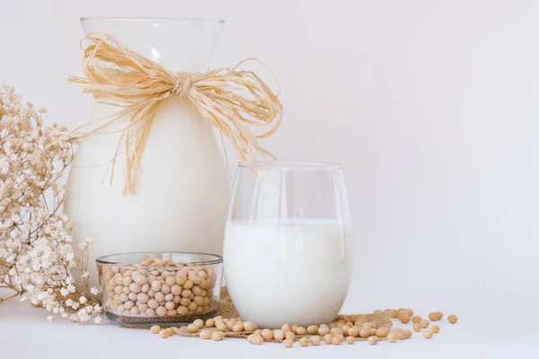 Leche de soja en un vaso y una jarra con semillas de soja crudas en whi — Foto de Stock