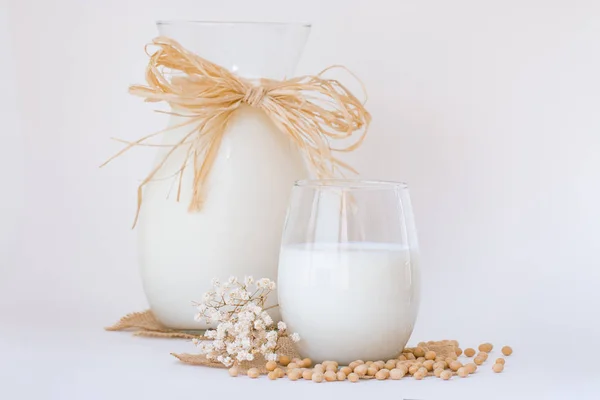 Leche de soja en un vaso y una jarra con semillas de soja crudas en whi — Foto de Stock