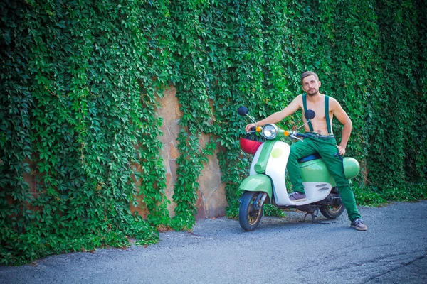 Young guy on a scooter against a wall of plants