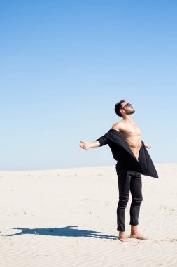 Siyah açılarak gömlekli adam kumun üzerinde duruyor