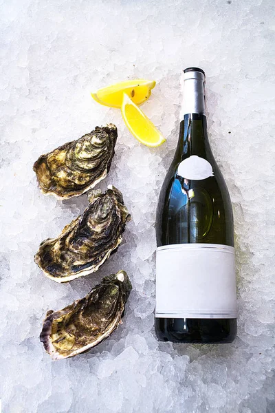 Tres grandes ostras hermosas se encuentran cerca de una botella de vino en el hielo — Foto de Stock