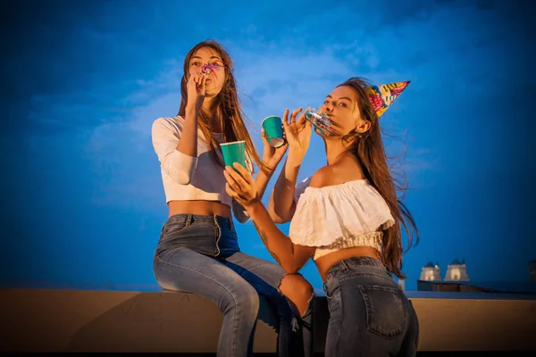 Zwei attraktive junge Frauen begrüßen und feiern den geblasenen Geburtstag der Trompete und heben die Hände — Stockfoto
