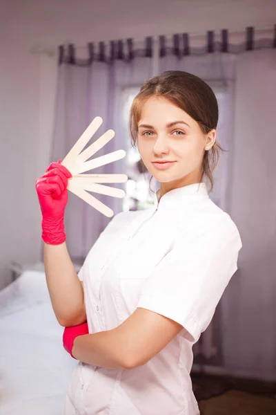 Kosmetolog i rosa handskar med trä spatlar — Stockfoto