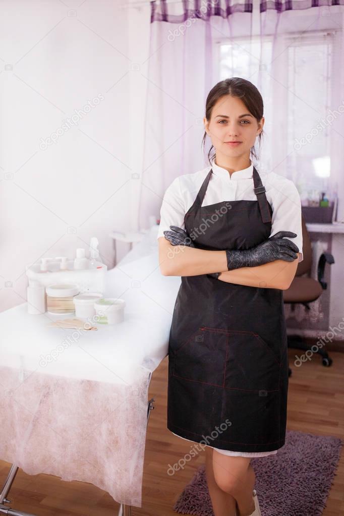 A beautician girl stands in a black apron and gloves