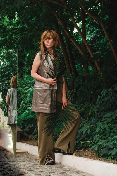 Egzotik kız bir fern iki yaprakları ile bir parkta duruyor