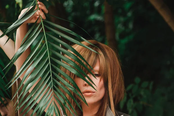 Ledsen flicka ser ner under en palm filial — Stockfoto