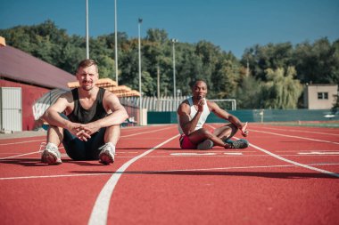 Beyaz bir sporcu ve bir lolipop siyah bir adamla stadyumda oturup