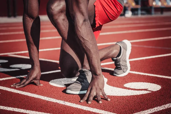 Hands and feet of a dark-skinned man on the track of the stadium