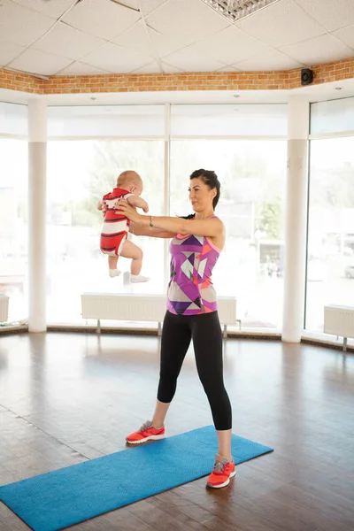Mom in the gym keeps the baby on arms outstretched