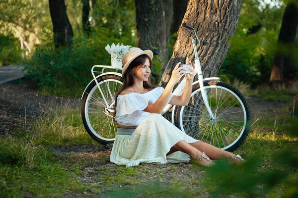 Uma menina senta-se na grama e tira uma foto no telefone — Fotografia de Stock