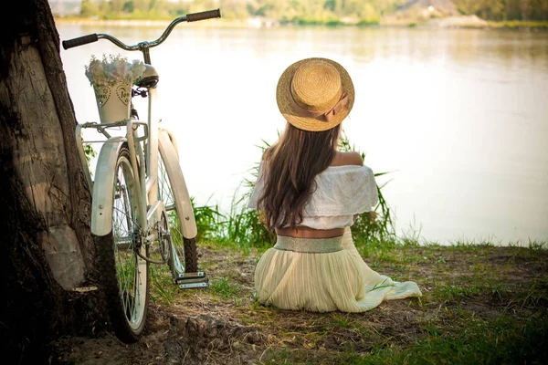 Вид сзади на девушку, сидящую на берегу и смотрящую на реку — стоковое фото