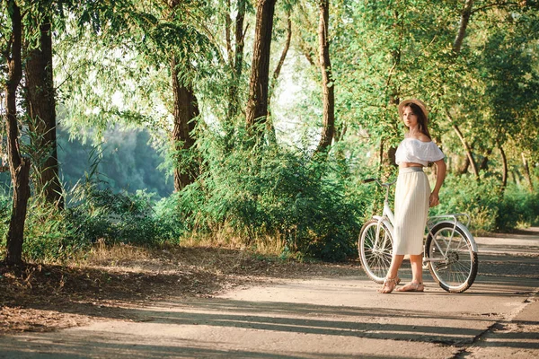 Uma menina está de pé apoiada em uma bicicleta no parque — Fotografia de Stock