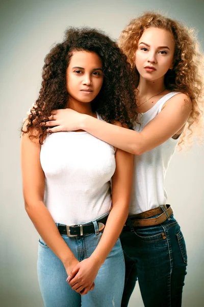 Σγουρά ξανθά και αφρικανική αμερικανική αγκαλιά στο τζιν και τις λευκές μπλούζες — Φωτογραφία Αρχείου