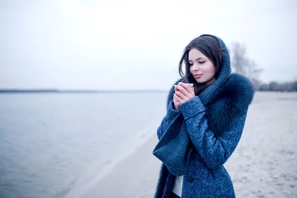 Hermosa chica de invierno en la orilla del río con un vaso de café —  Fotos de Stock