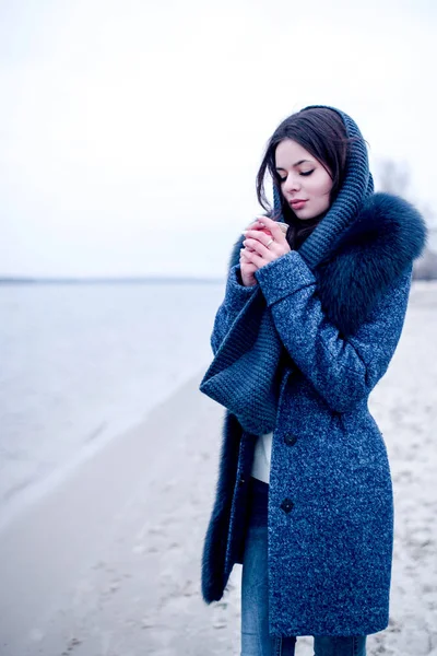 Bella ragazza invernale sulla riva del fiume con un bicchiere di caffè — Foto Stock