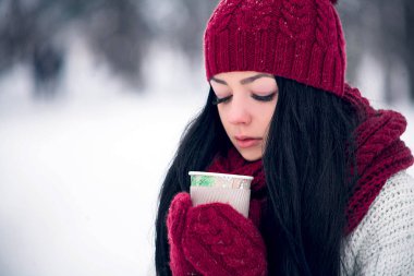 Güzel genç bir kadın beyaz bir kazak ve parlak bir şapka, eşarp ve eldiven bir bardak kahve ile