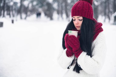 Güzel genç bir kadın beyaz bir kazak ve parlak bir şapka, eşarp ve eldiven bir bardak kahve ile