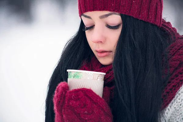 Una bella giovane donna in un maglione bianco e un cappello luminoso, sciarpa e guanti con un bicchiere di caffè — Foto Stock