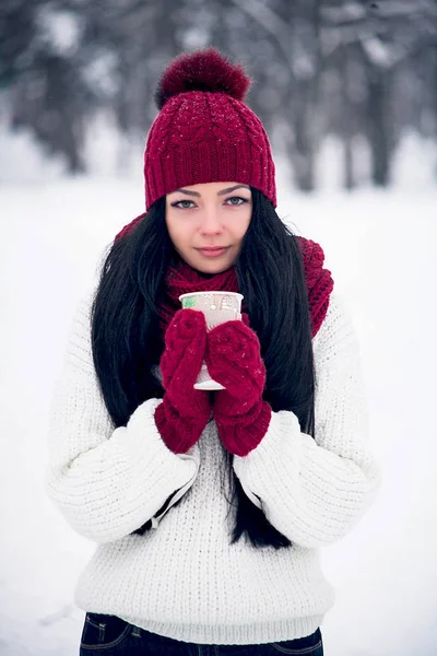 Een mooie jonge vrouw in een witte trui en een heldere muts, sjaal en wanten met een glas van koffie Stockafbeelding