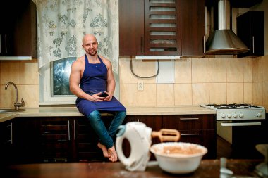 Apronda genç bir adam mutfakta oturuyor