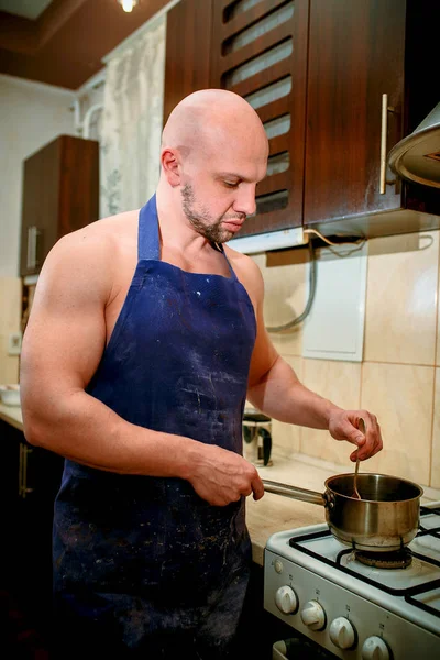 A young man chef stands behind a stove — Stock Photo, Image