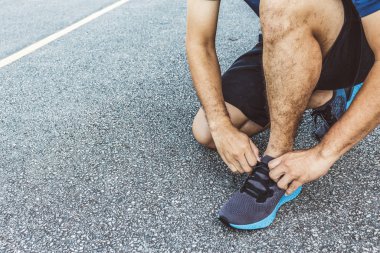 Yakın plan sporcusu arka planda hafif odaklı ve ışığın üzerinde koşu ayakkabıları bağlıyor