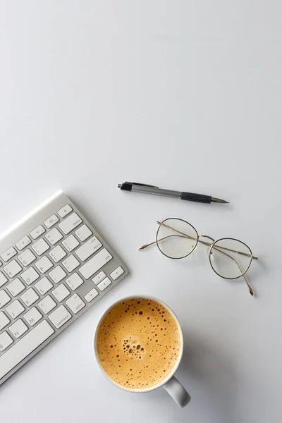 business concept. top view of office desk workspace with keyboard, pen, glasses and hot coffee cup on white table background. over light
