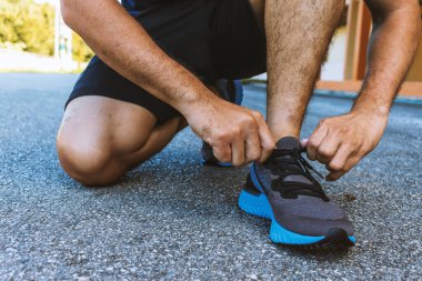 Yakın plan sporcusu arka planda hafif odaklı ve ışığın üzerinde koşu ayakkabıları bağlıyor