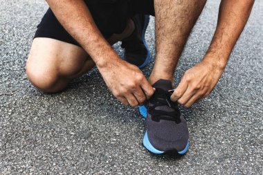 Yakın plan sporcusu arka planda hafif odaklı ve ışığın üzerinde koşu ayakkabıları bağlıyor