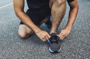 Yakın plan sporcusu arka planda hafif odaklı ve ışığın üzerinde koşu ayakkabıları bağlıyor