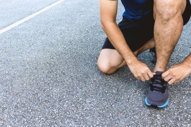 Yakın plan sporcusu arka planda hafif odaklı ve ışığın üzerinde koşu ayakkabıları bağlıyor