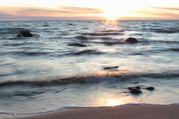 海での静かな夜のロマンチックな雰囲気 波のある滑らかな海から突き出た石 最後の太陽光線とオレンジの地平線 海と岩のソフトフォーカス長時間露光 — ストック写真