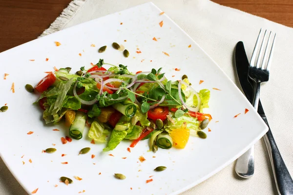 Salade met verse groenten, pompoenpitten, sinaasappelen op de witte plaat — Stockfoto