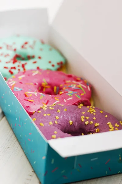 Bunte Donuts in der Schachtel auf weißem Holzhintergrund — Stockfoto