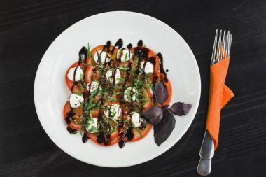 Turuncu bir peçeteye aygıtlarla beyaz tabakta Caprese salatası