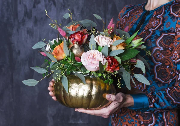 Autumn floral bouquet in pupkin vase. Floral decoration in woman hands