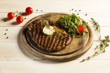 Tereyağı ile sığır eti biftek ızgara ve roket bir yuvarlak tahta üzerinde yapraklar