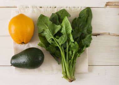 Demet taze ıspanak, turuncu ve Beyaz ahşap zemin üzerinde avokado