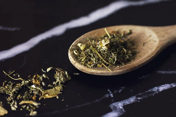 Травяной чай в деревянной ложке на черном мраморном фоне — стоковое фото