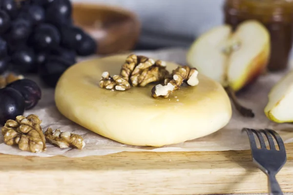 Queijo, mel, uvas, peras e nozes em tábua de madeira na cozinha — Fotografia de Stock