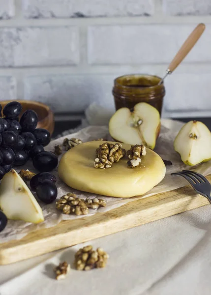 Queijo, mel, uvas, peras e nozes em tábua de madeira — Fotografia de Stock