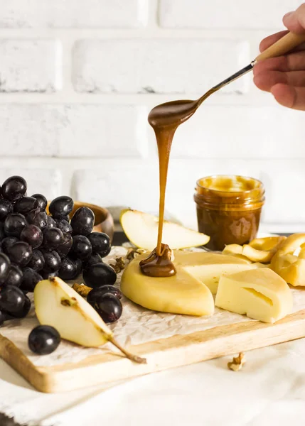 O mel flui da colher para o queijo na tábua de madeira com frutas — Fotografia de Stock