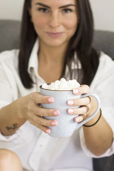 Glimlachend brunette meisje in wit overhemd zittend op de Bank met mok in handen — Stockfoto