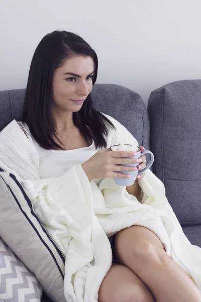 Jonge vrouw in deken met Cup van cacao zittend op de Bank en Tv kijken — Stockfoto