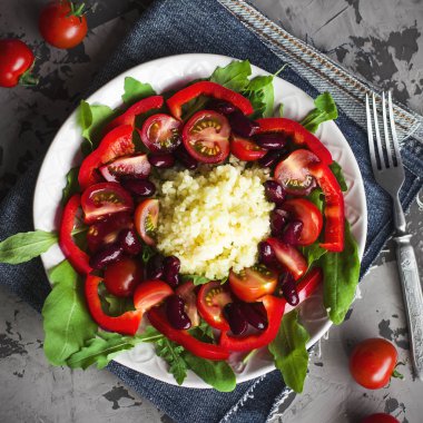 Roka, domates, biber ve koyu gri beton zemin üzerine beyaz tabak içinde kırmızı fasulye kuskus salatası